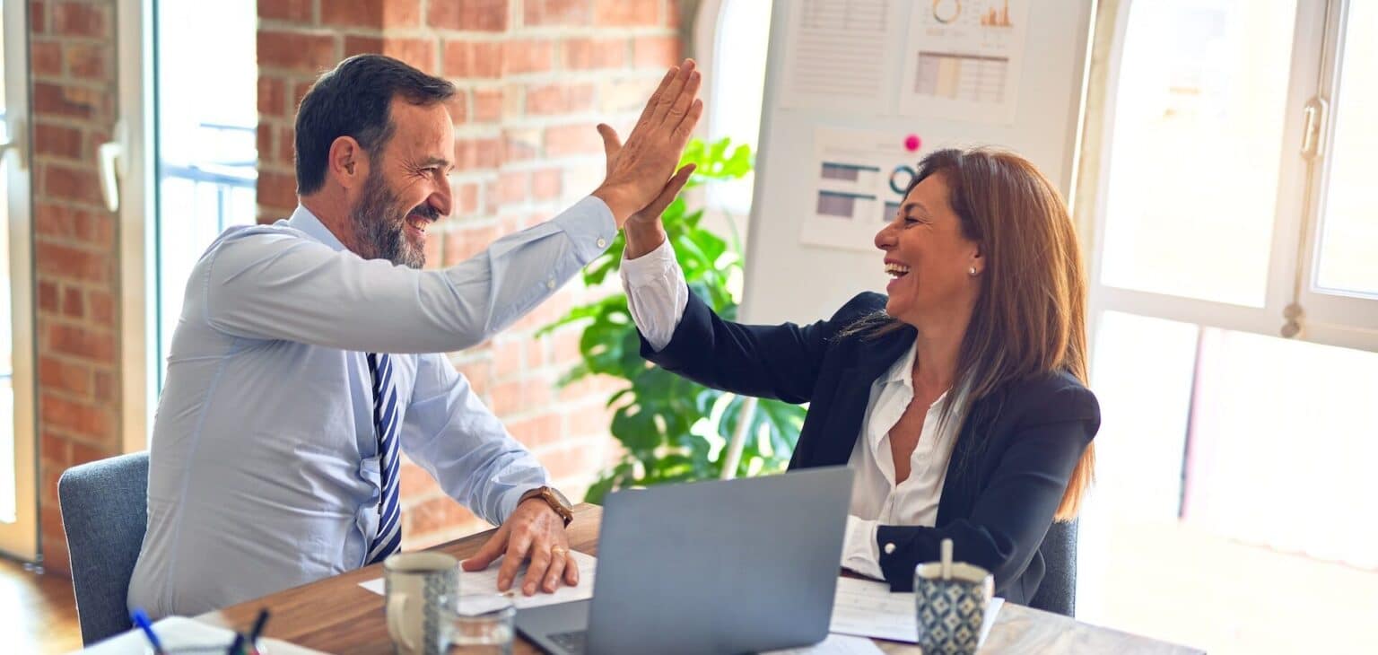 Business English Courses: Two happy business people high fiving after a successful business English course. / Zakelijk Engels cursussen.